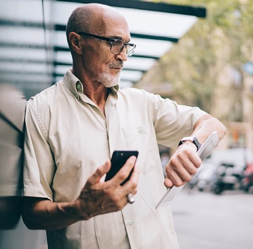 old man looking using his phone and looking at his wrist watch for time